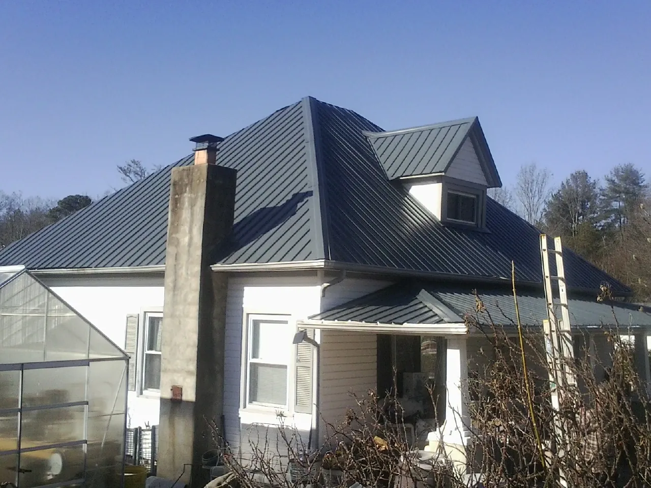 Dark blue standing seam metal roof on a white farmhouse with dormer — Slate & Tile Roof Repair by Roofing Brothers in Latimer
