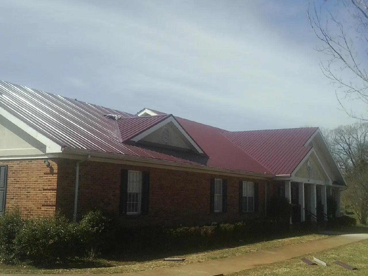 Red metal roof with gabled entries on a long brick building, from a Hail Damage Roof Repair job in Latimer