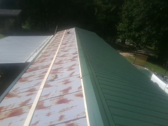 Old rusted panels beside newly installed green metal roofing — Wind Damage Roof Repair by Roofing Brothers in Latimer