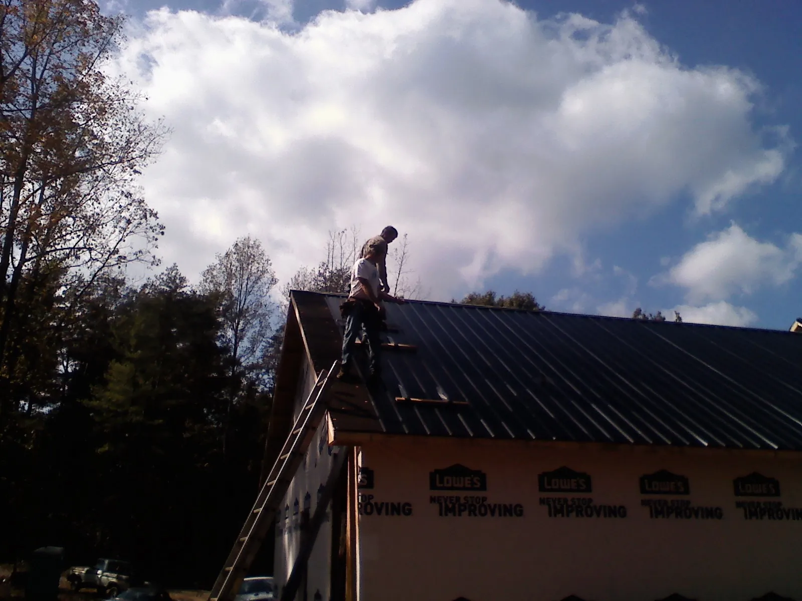 Roofer fastening dark metal panels high against a cloudy sky, from a Roof Inspection job in Latimer