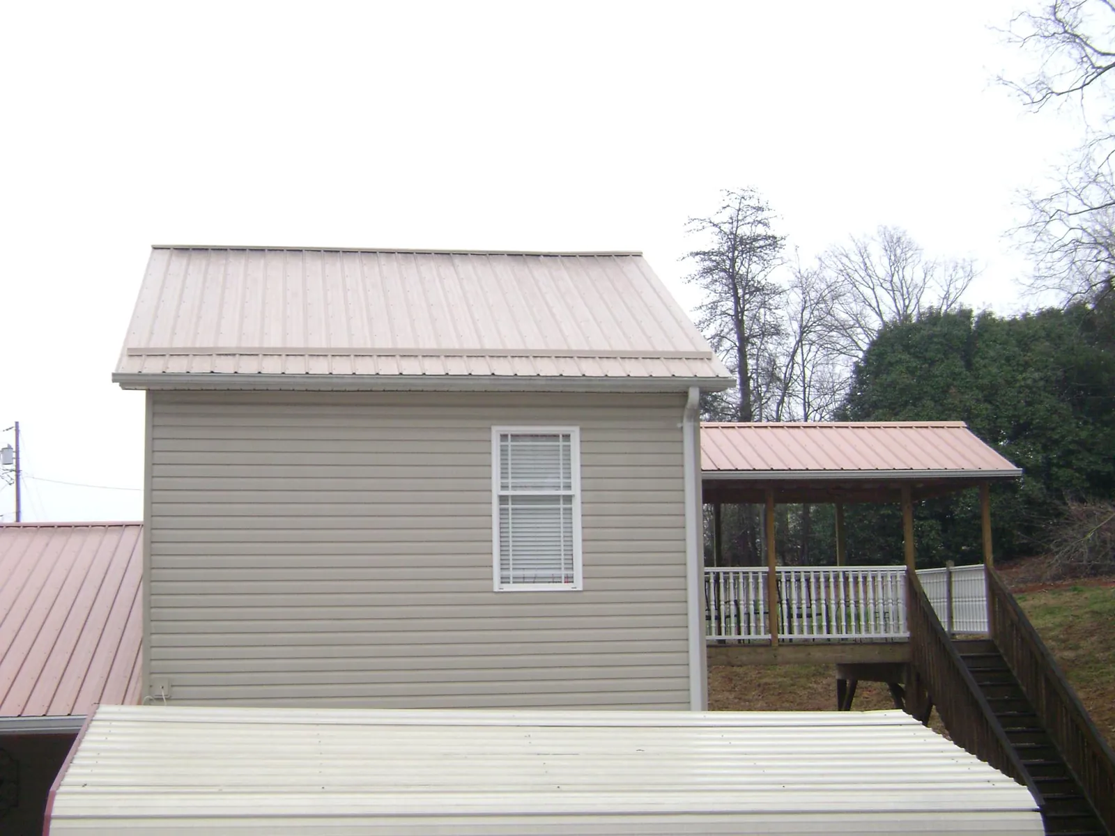 Tan metal roofs on a two story addition and attached porch, from a Roof Replacement job in Latimer